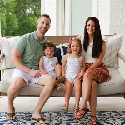Chiropractor Rogers AR Taylor Elder With Fmaily Meet The Team Doctor Taylor with their wife and two small children. They are sitting on an tan couch outside